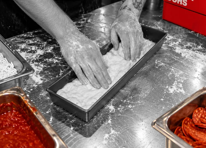 Hands pressing Dough Dohs 72-hour fermented sourdough into a pizza pan